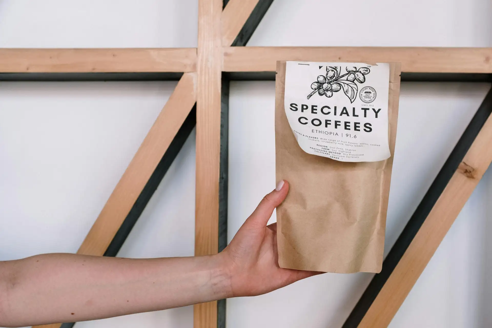 A person's hand holding a brown kraft paper coffee bag with a white 